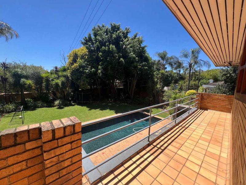 An elevated balcony with tiled flooring and metal railings, overlooking a private swimming pool and a well-maintained garden area.