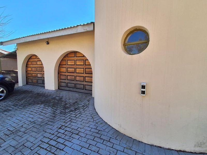 Exterior view of a property featuring a double garage with arched wooden doors, a distinctive circular window, and a paved driveway.