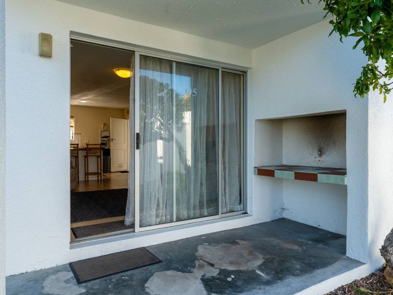 Covered patio area featuring a built-in braai, concrete flooring, and sliding glass door access to the interior living space.
