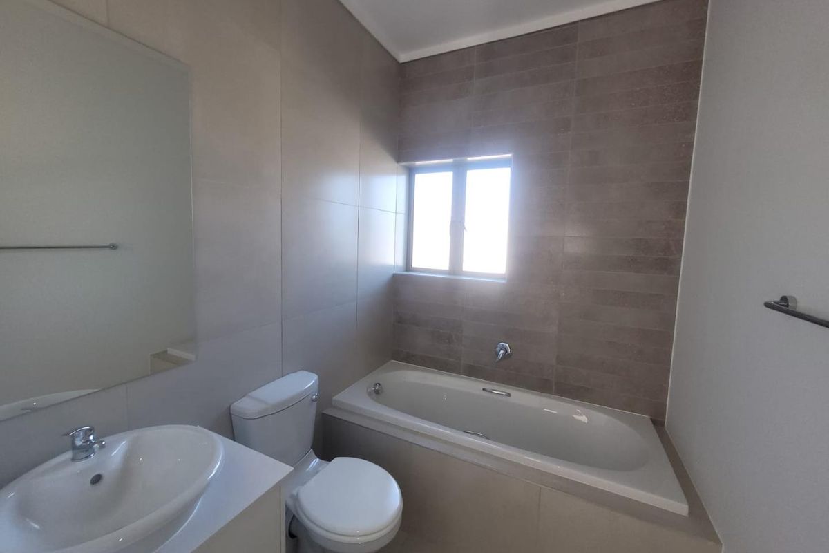 A modern bathroom featuring a built-in bathtub, a vanity with a basin, a toilet, and neutral wall tiling.