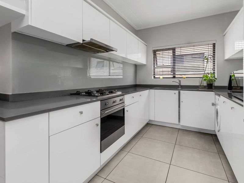 Modern kitchen featuring sleek white cabinetry, stone countertops, integrated gas hob, oven, extractor fan, and tiled flooring with a neutral glass splashback.