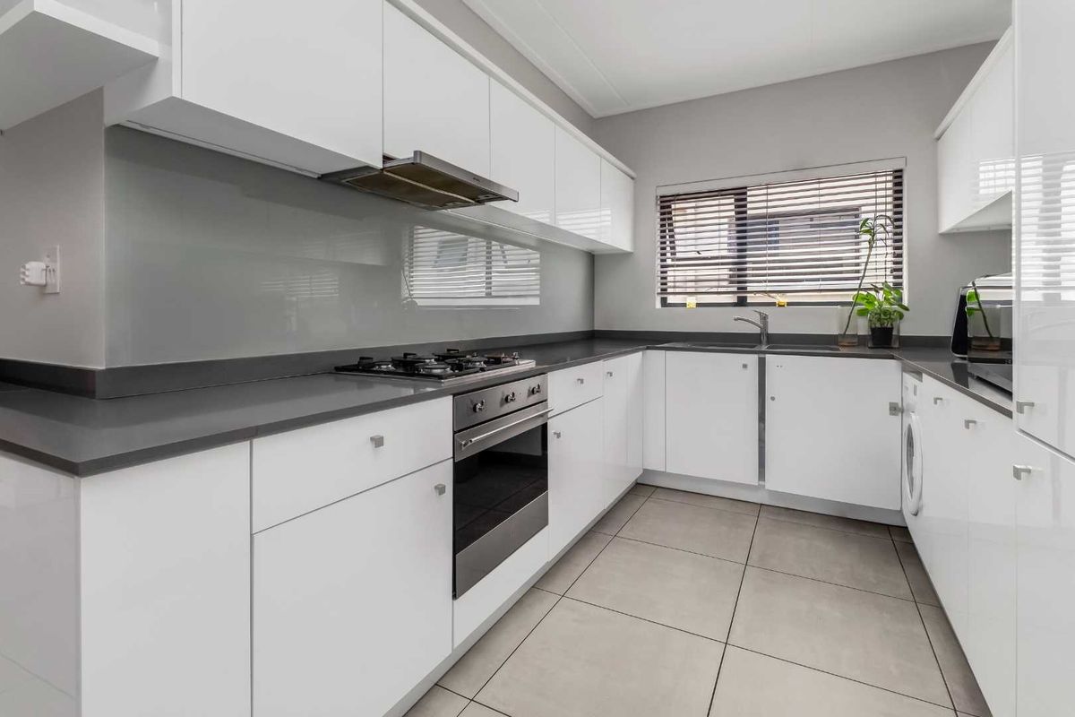 Modern kitchen featuring sleek white cabinetry, stone countertops, integrated gas hob, oven, extractor fan, and tiled flooring with a neutral glass splashback.