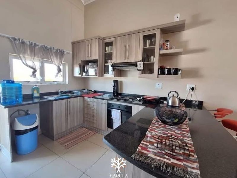 Modern kitchen featuring light wood-grain cabinetry, granite countertops, a breakfast bar, and integrated appliances, offering a functional and contemporary cooking space.