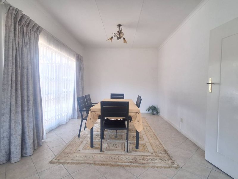 A bright dining room featuring tiled flooring, a ceiling light fixture, and a sliding door with security gate access to the exterior.