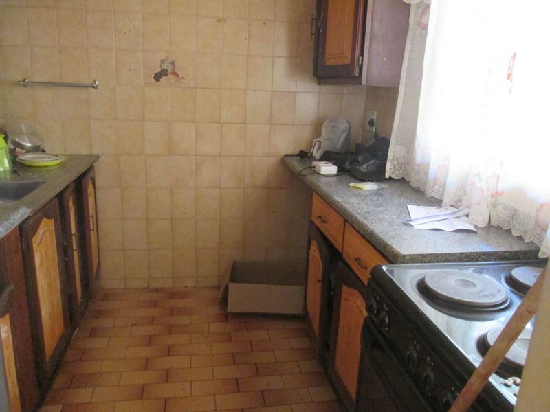 A dated kitchen featuring built-in cabinetry, tiled backsplash, stone-look countertops, and an electric stove, offering potential for a modern renovation.