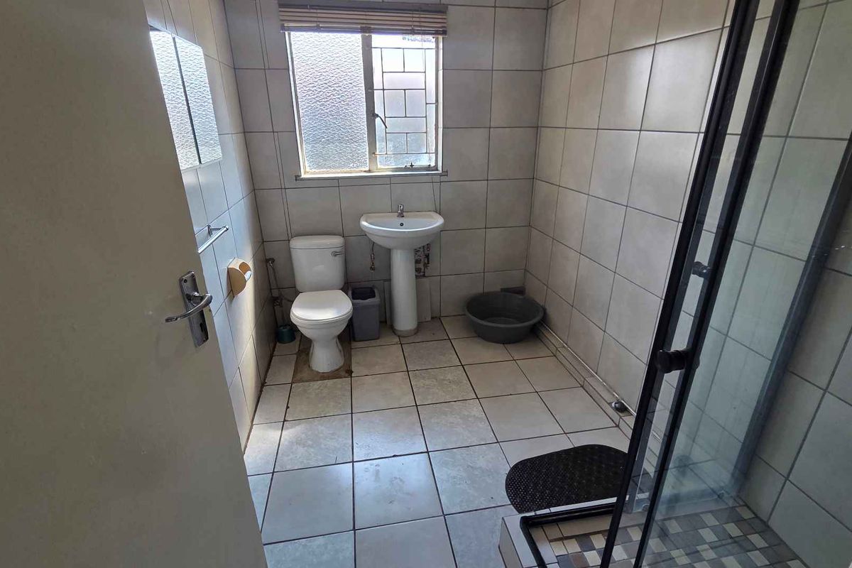 A functional bathroom featuring a pedestal basin, toilet, and a glass-enclosed shower with tiled walls and flooring.