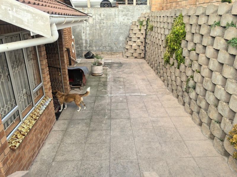 A rear exterior area featuring a paved patio, brick walling, and a large concrete block retaining wall.