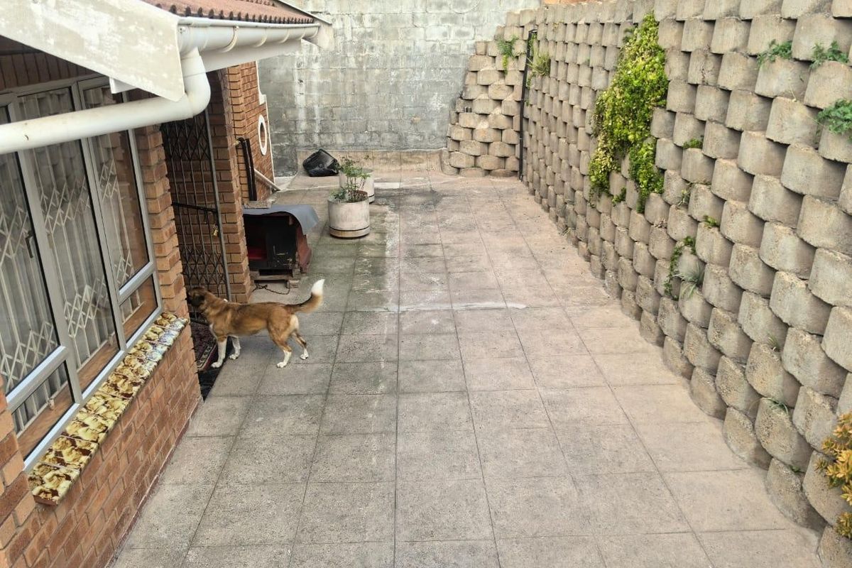 A rear exterior area featuring a paved patio, brick walling, and a large concrete block retaining wall.