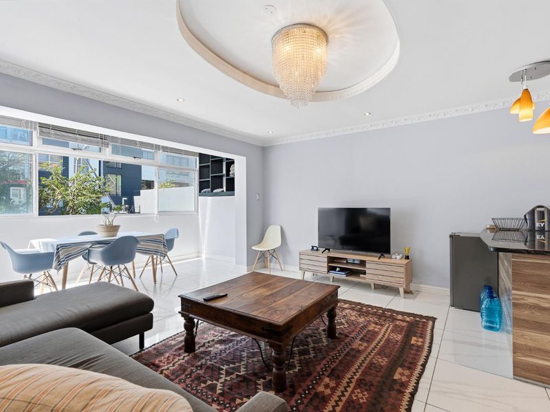 Spacious open-plan living and dining area featuring tiled floors, decorative crown molding, a recessed ceiling with a crystal chandelier, and large windows.
