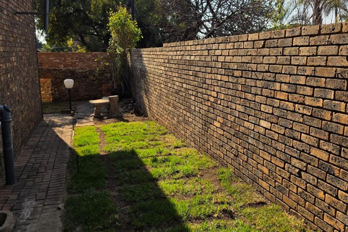 A side garden area featuring a paved walkway and a high face brick boundary wall, providing a private outdoor space.