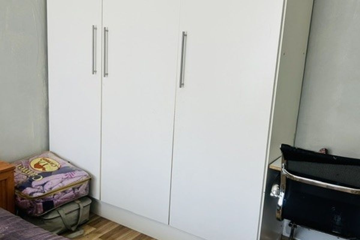A bedroom featuring a large white built-in wardrobe and wood-look laminate flooring.