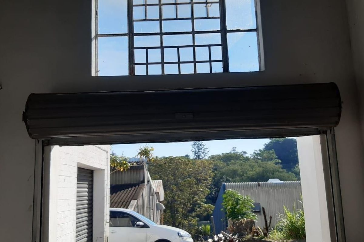 Industrial utility space featuring a high-level steel-framed window and a functional roller shutter door, providing access to the exterior yard area.