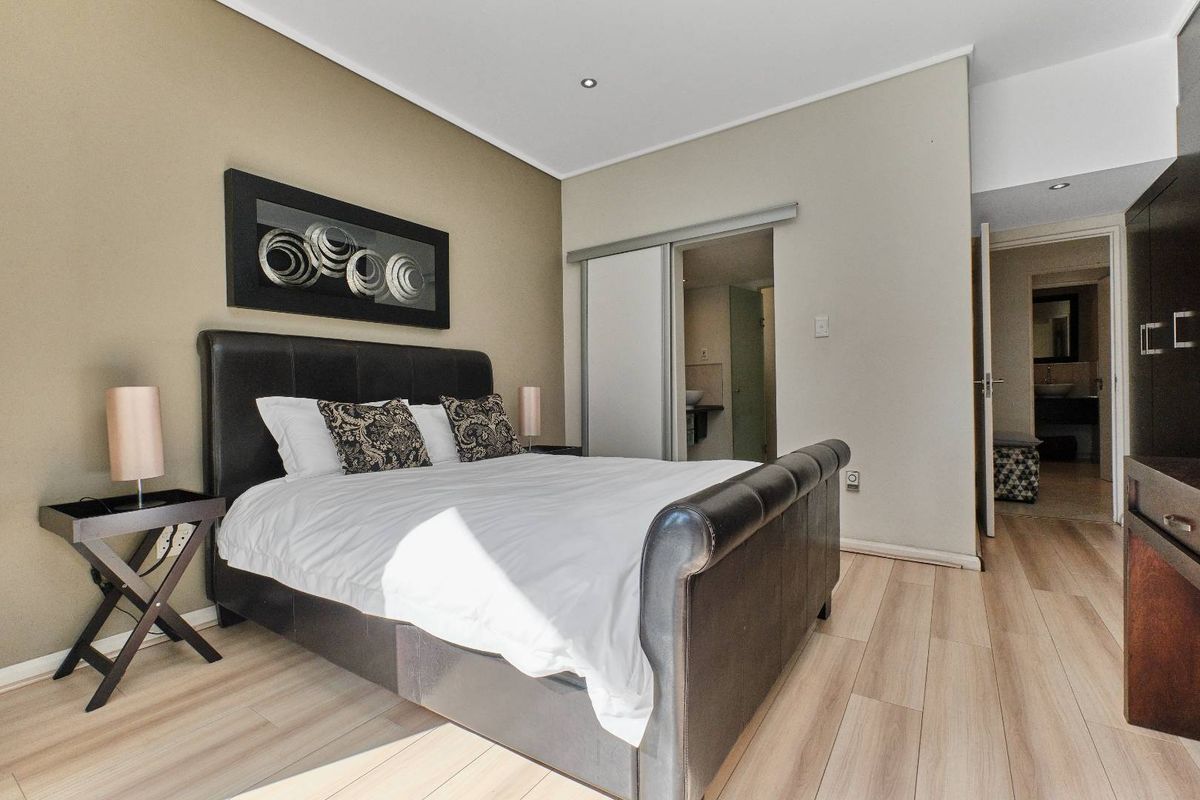 A well-maintained bedroom featuring light wood-look flooring, recessed ceiling lighting, and an en-suite bathroom with a sliding door entrance.