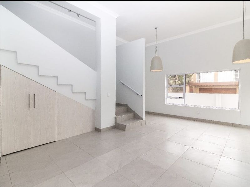 Bright and spacious open-plan living area featuring neutral tiled flooring, under-stair storage cabinetry, and modern pendant lighting.