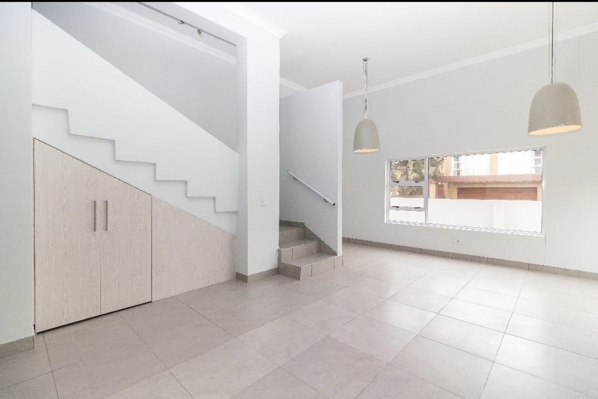 Bright and spacious open-plan living area featuring neutral tiled flooring, under-stair storage cabinetry, and modern pendant lighting.