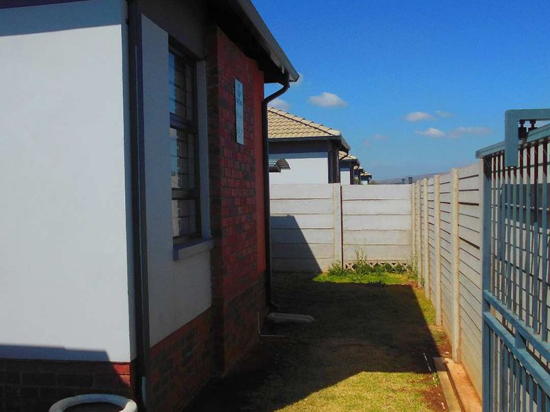 A side view of the property showing a brick and plaster exterior, a precast concrete boundary wall, and a metal security gate.