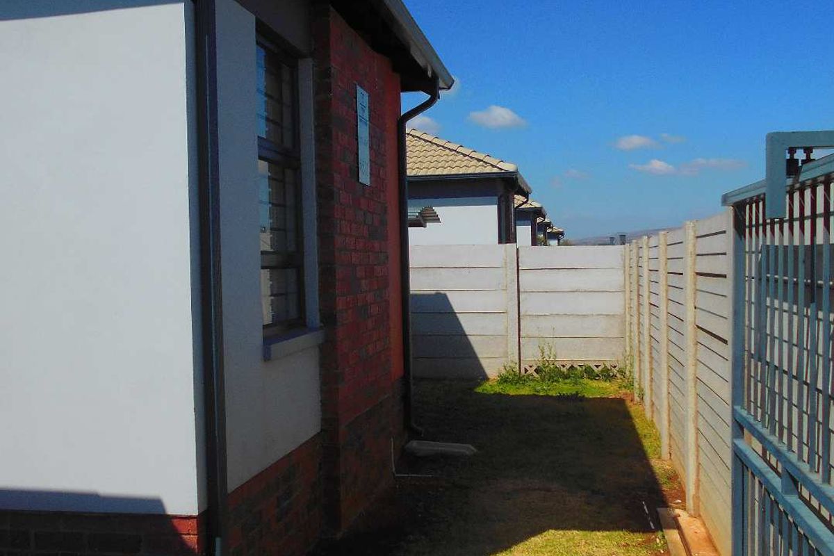 A side view of the property showing a brick and plaster exterior, a precast concrete boundary wall, and a metal security gate.