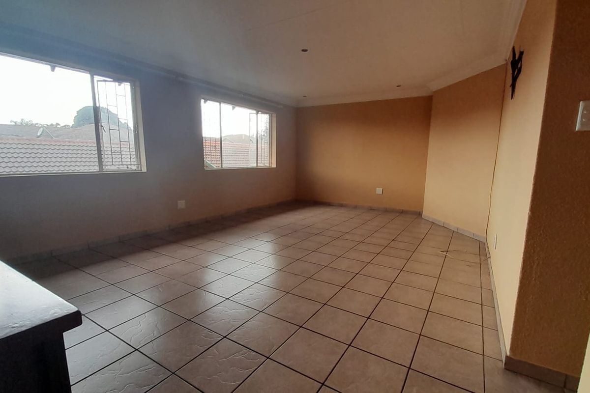 A spacious, empty living area featuring tiled flooring, neutral walls, and large windows providing natural light.