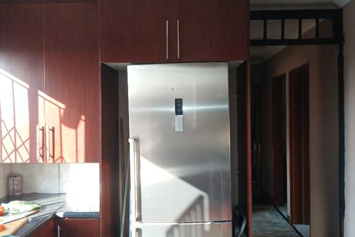 A functional kitchen area featuring dark wood-finish built-in cabinetry, tiled flooring, and a dedicated space for a refrigerator, leading into a hallway.