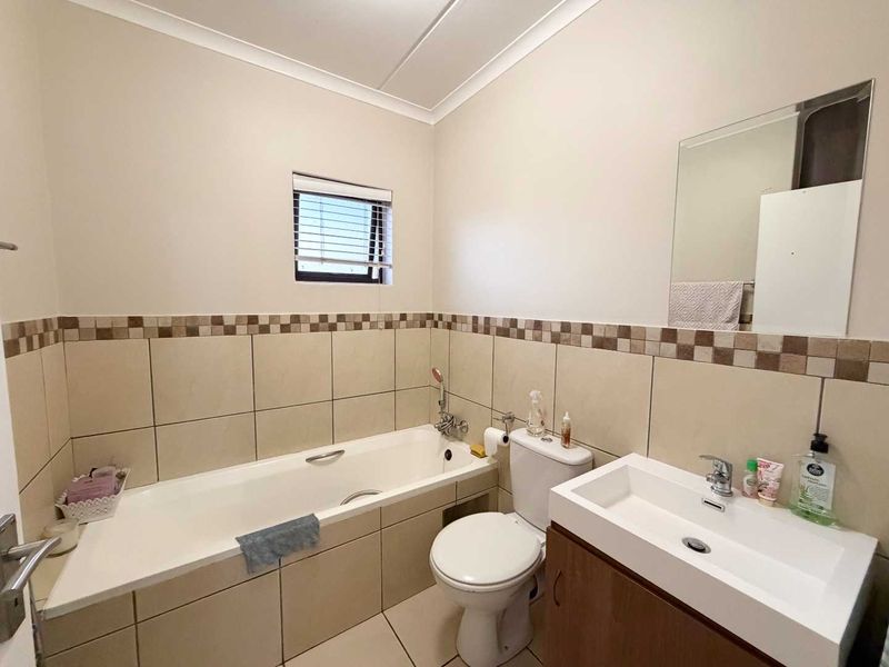 A functional bathroom featuring a bathtub, toilet, and vanity basin with tiled splashbacks and a wall-mounted mirror.