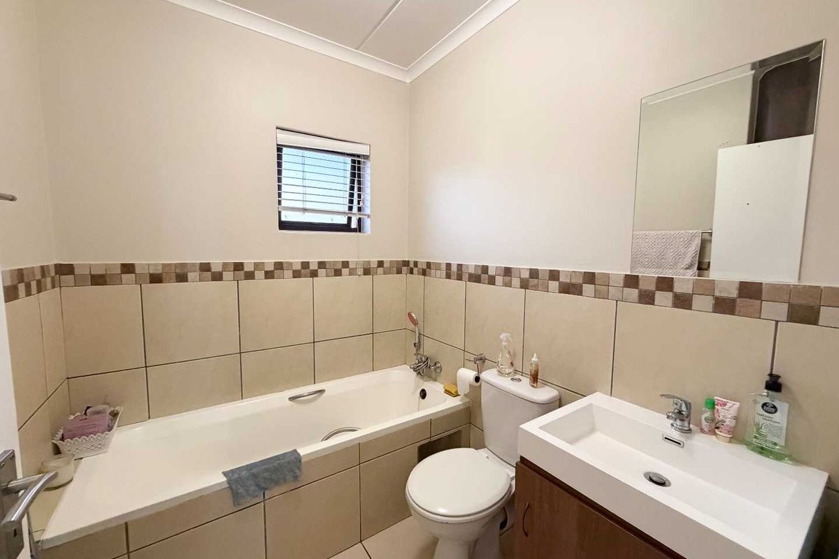 A functional bathroom featuring a bathtub, toilet, and vanity basin with tiled splashbacks and a wall-mounted mirror.