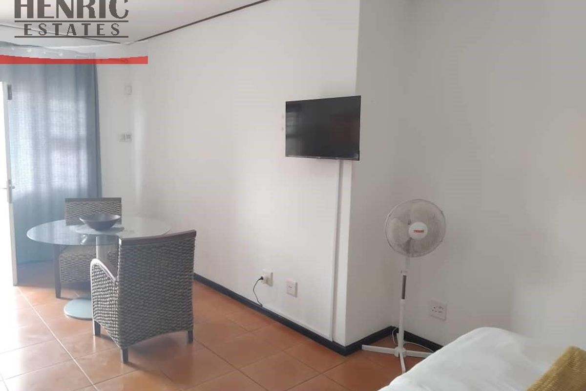A functional living area featuring tiled flooring, wall-mounted television, and access to an outdoor space through a glass door.