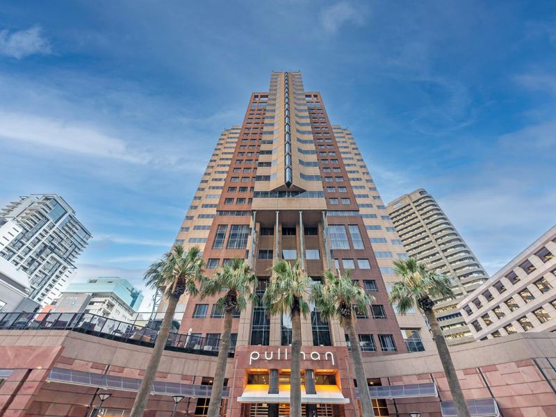 A low-angle exterior view of a modern high-rise apartment building facade featuring architectural cladding and a prominent entrance canopy.