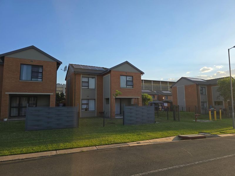A view of the front facade of a brick townhouse complex featuring solar panels, private fencing, and well-maintained lawn areas.