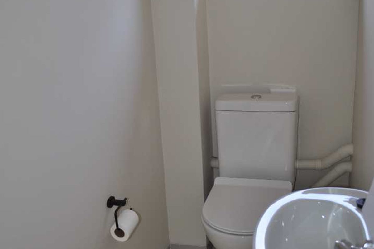 A clean and functional office bathroom featuring a white toilet, pedestal basin, and neutral tiled flooring.