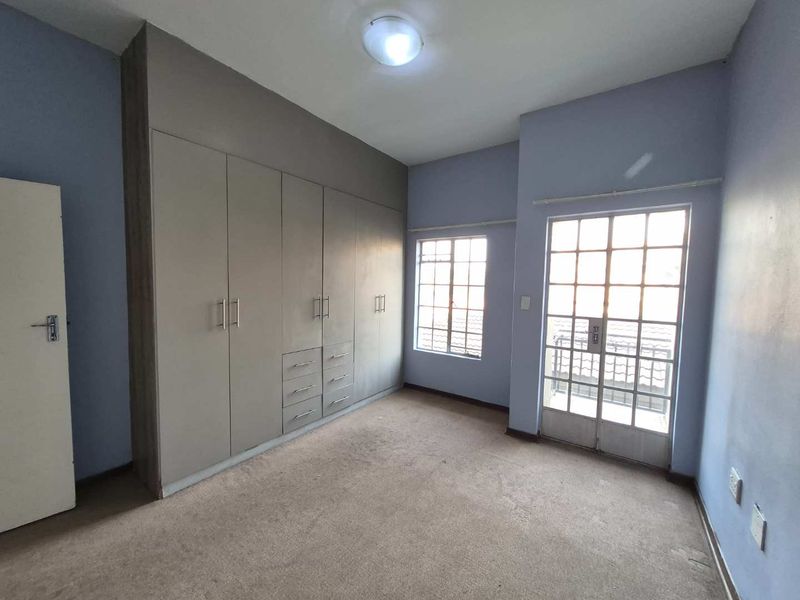 An empty bedroom featuring built-in cupboards, carpeted flooring, and a glass-paned door leading to an outdoor area.