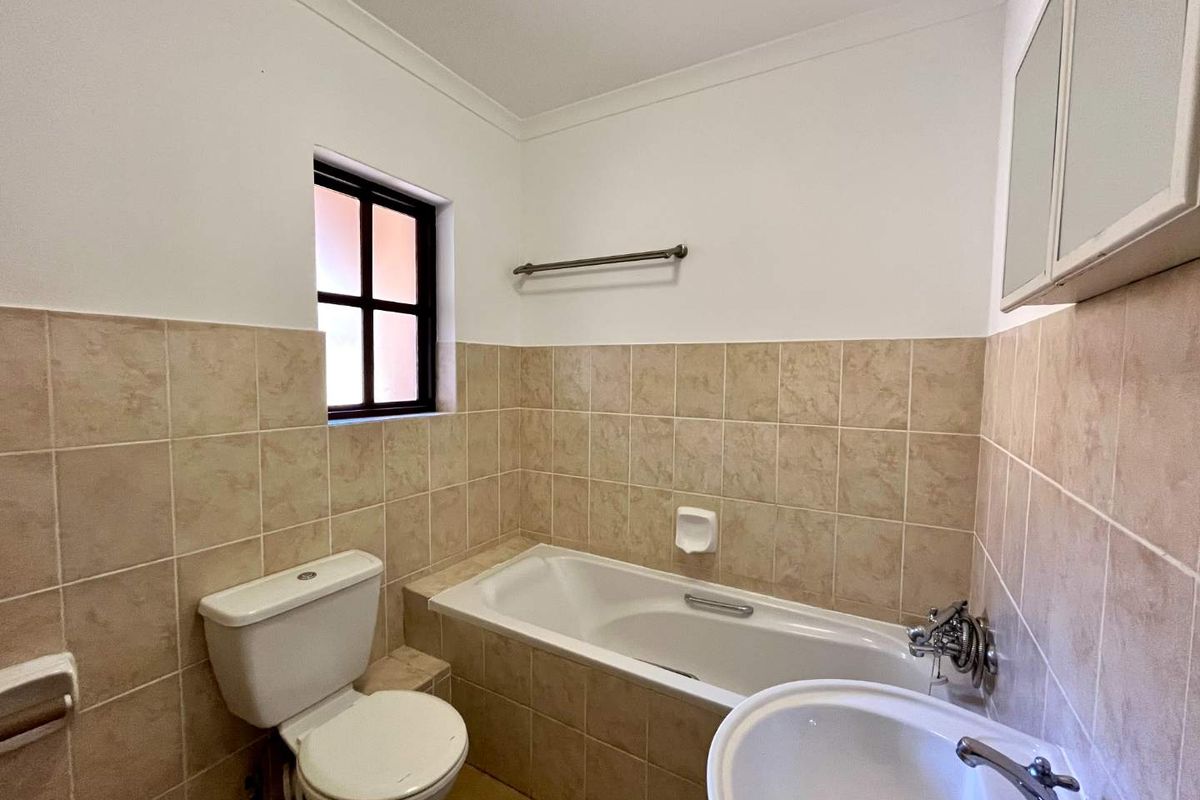 A functional bathroom featuring a bathtub, pedestal basin, and toilet with neutral wall tiling and a window for natural light.