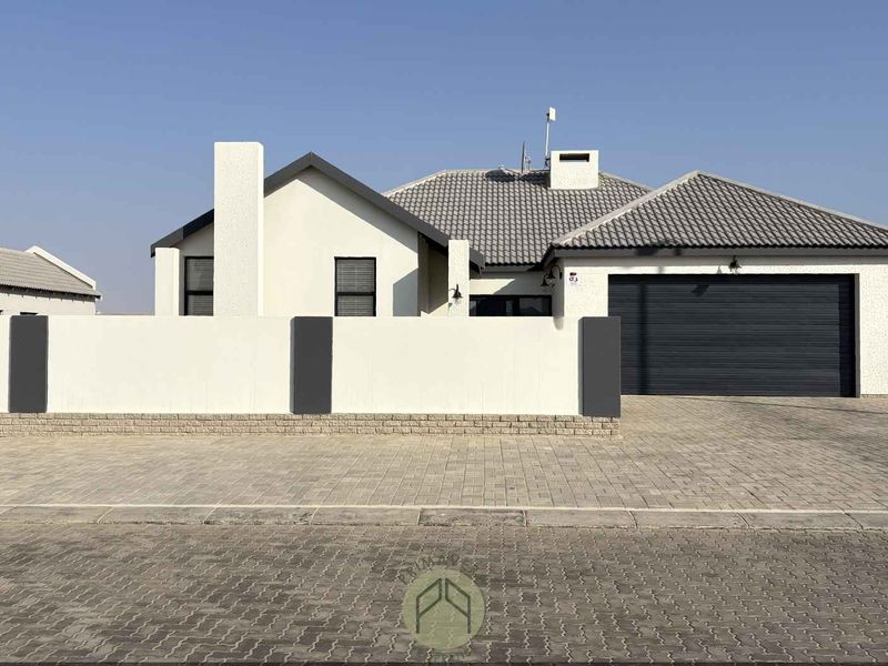 A modern single-story house featuring a tiled roof, a double garage, and a clean, paved driveway behind a secure boundary wall.