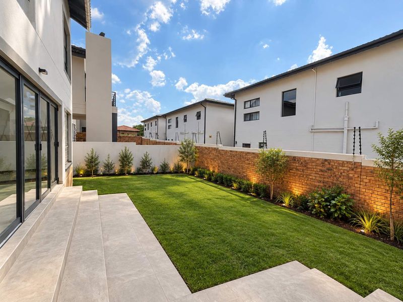 A well-maintained rear garden featuring a tiled patio, manicured lawn, and brick boundary walls with integrated lighting and electric fencing.