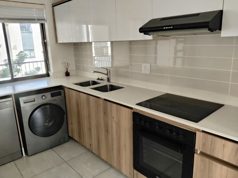 Modern kitchen featuring sleek wood-finish cabinetry, stone countertops, integrated appliances including an oven and hob, and a clean tiled backsplash.