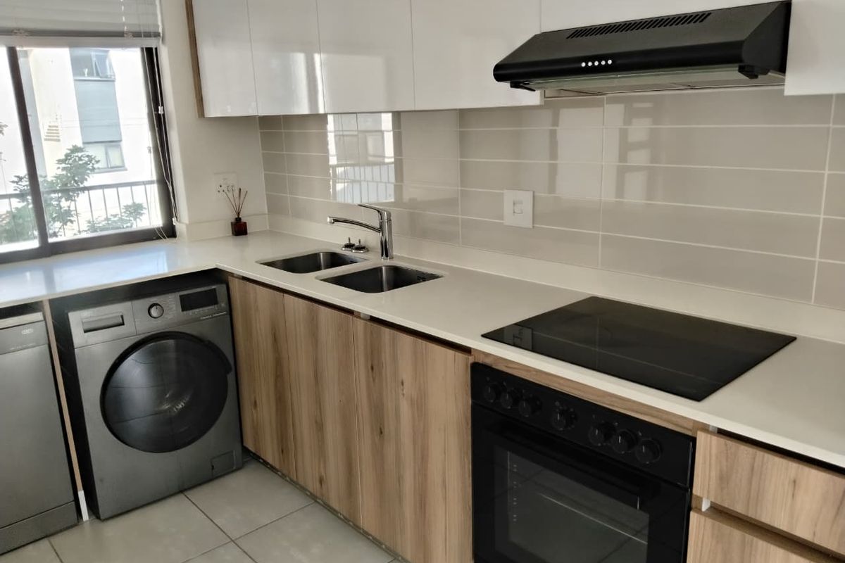 Modern kitchen featuring sleek wood-finish cabinetry, stone countertops, integrated appliances including an oven and hob, and a clean tiled backsplash.
