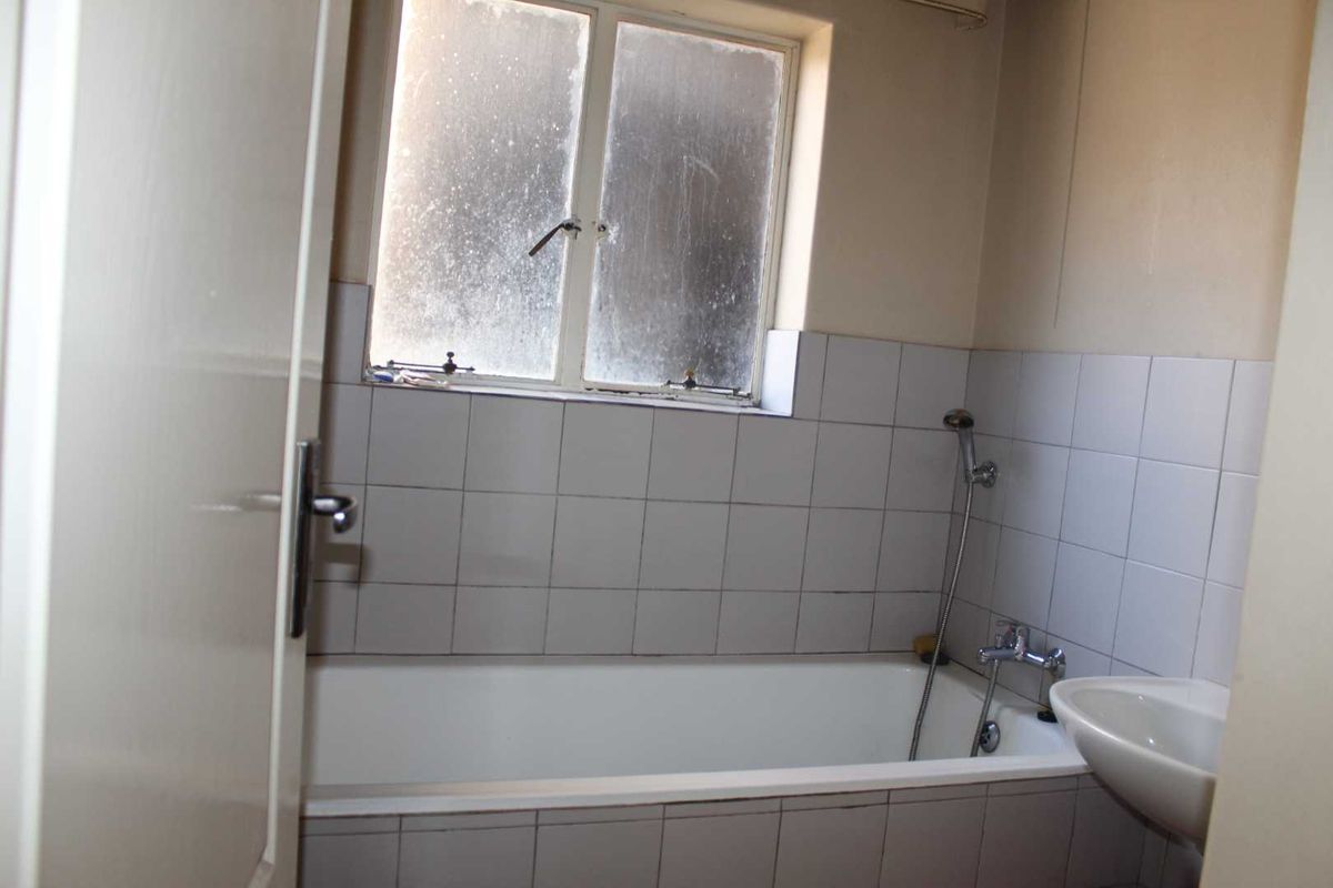 A functional bathroom featuring a bathtub with a handheld shower attachment, a wall-mounted basin, and tiled splashbacks under a casement window.