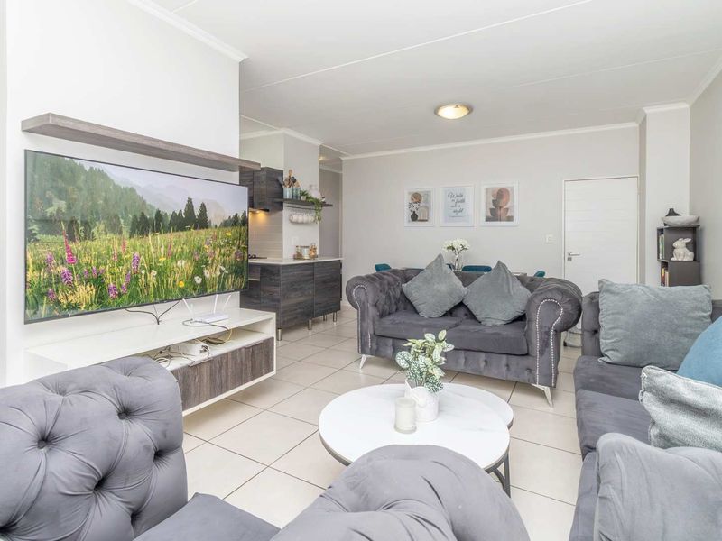 An open-plan living and kitchen area featuring neutral tiled flooring, modern cabinetry, and a bright, well-maintained interior layout.