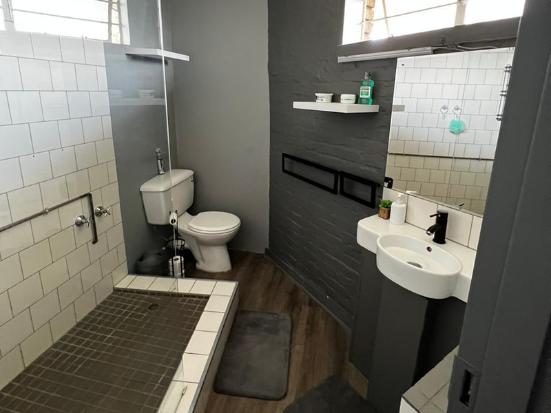 Modern bathroom featuring a walk-in shower with subway tiling, a pedestal basin, and a toilet, finished with dark grey walls and laminate flooring.