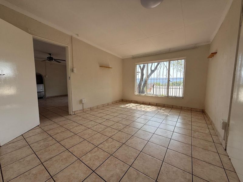 An empty living room featuring tiled flooring, a large window with security bars, and neutral wall tones, offering a blank canvas for interior design.