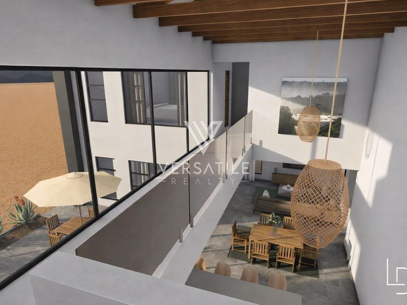 A modern double-volume open-plan living and dining area featuring exposed timber beams, large glass windows, and a sleek glass balustrade overlooking the space.