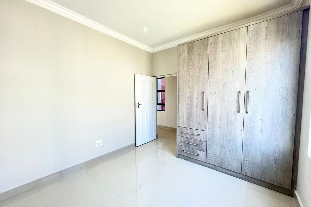 A bright, empty bedroom featuring neutral tiled flooring, crown molding, and modern built-in wooden wardrobes.