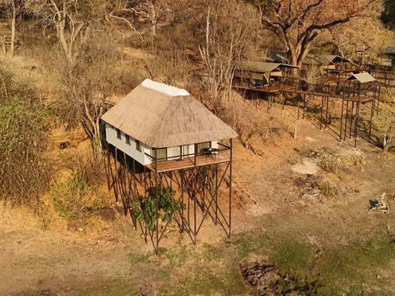 Aerial view of an elevated lodge unit featuring a thatched roof and timber deck, set within a natural bushveld landscape.