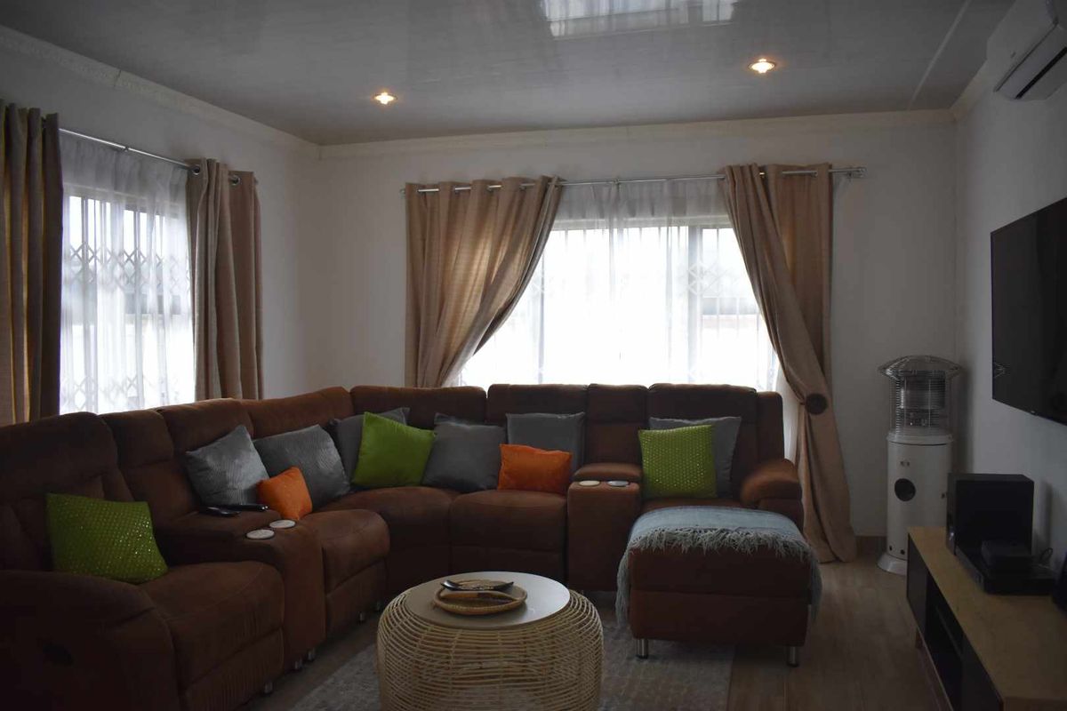 A comfortable living room featuring recessed ceiling lighting, wall-mounted air conditioning unit, and large windows with security bars.