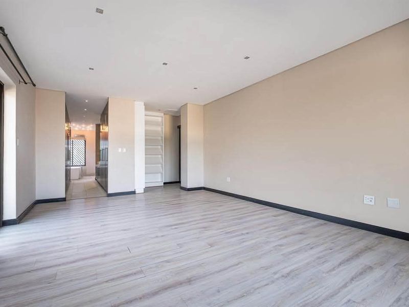 A spacious, empty living area featuring modern laminate flooring, recessed downlighting, and a sliding glass door leading to an outdoor space.