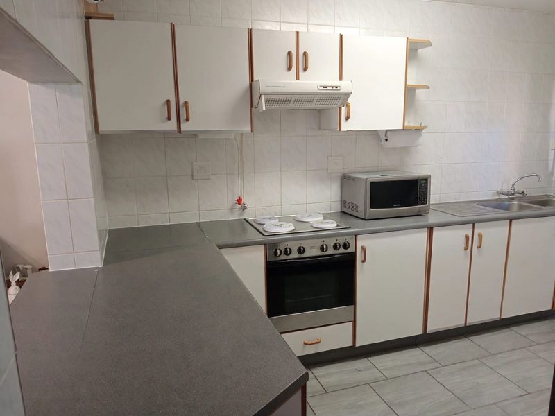 Functional kitchen featuring built-in cabinetry, laminate countertops, stainless steel sink, and integrated oven with extractor fan, finished with tiled splashbacks and flooring.