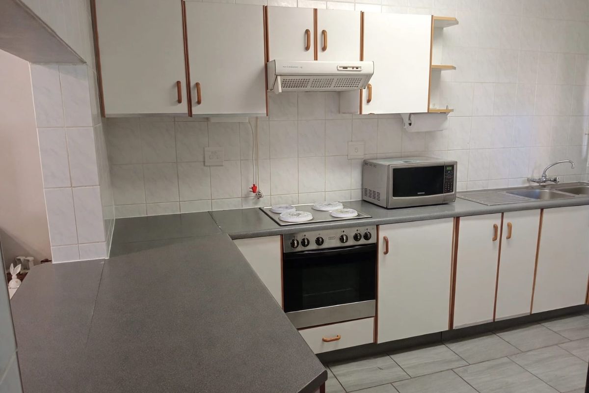Functional kitchen featuring built-in cabinetry, laminate countertops, stainless steel sink, and integrated oven with extractor fan, finished with tiled splashbacks and flooring.