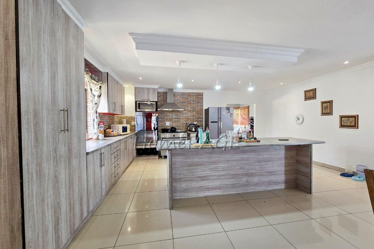 Modern open-plan kitchen featuring light wood-grain cabinetry, a central island, tiled flooring, and a brick-accented wall with a stainless steel extractor fan.