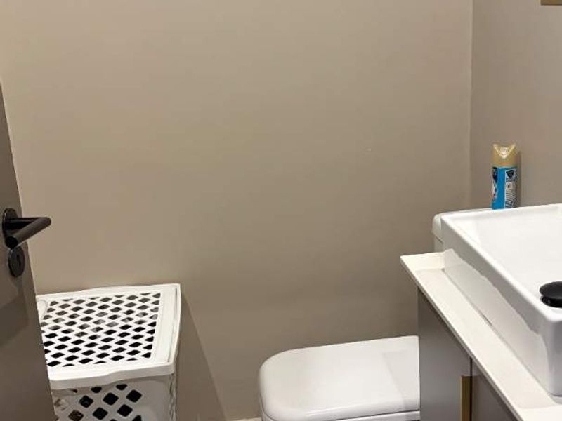 A compact bathroom featuring a modern vanity with basin, a white toilet, and neutral floor tiling.