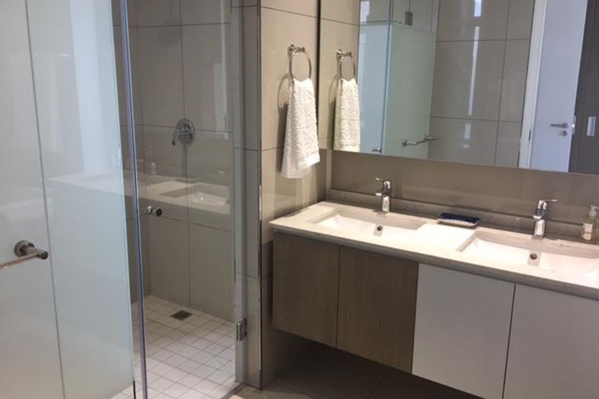 Modern bathroom featuring a double vanity with stone countertop, large wall-mounted mirror, and a separate glass-enclosed shower with neutral tiling.