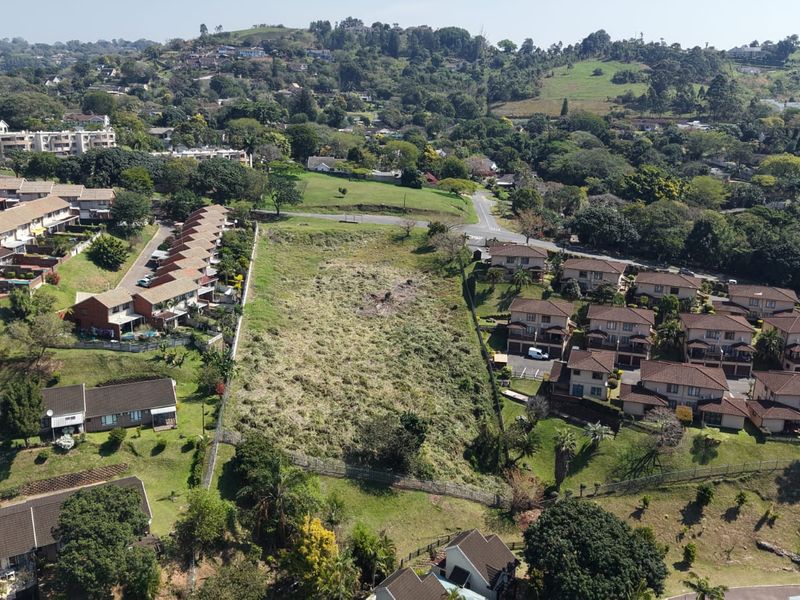 An aerial view of a vacant residential plot situated within an established suburban neighborhood, surrounded by existing residential developments.